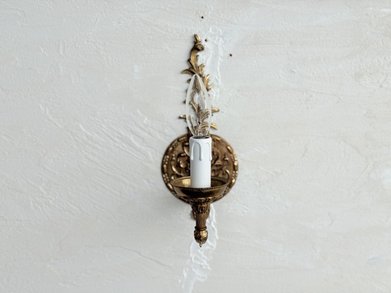 壁面に設置された、優雅なアームが特徴的な真鍮製ウォールランプの正面写真