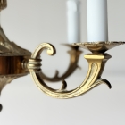 真鍮の鈍い光沢と剥がれかけた白いペイントの風合いが美しい、シャンデリアの曲線的なアーム部分。