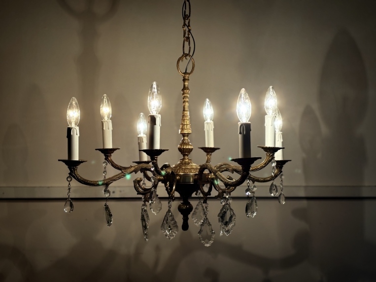 8灯すべての電球を点灯させた状態。温かみのある光が真鍮を照らし、壁に幻想的な影を落とす様子