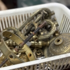 カゴに入れられた分解状態の真鍮パーツ類。経年による深い風合いと重厚な素材感が伝わるディテール