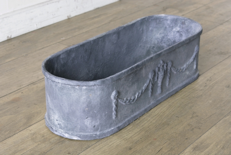 横幅595mmの使い勝手の良いサイズ感が魅力のアイアンプランター。シャビーシックなインテリアやアンティークガーデンに馴染む落ち着いた佇まいで、ショップの軒先を彩るディスプレイとしても映える一品。